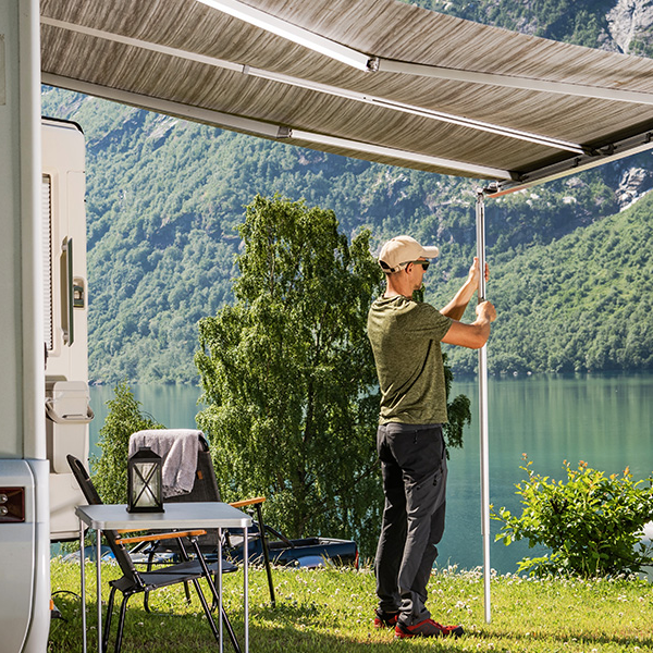 Man setting up an RV awning beside a scenic lake and mountains