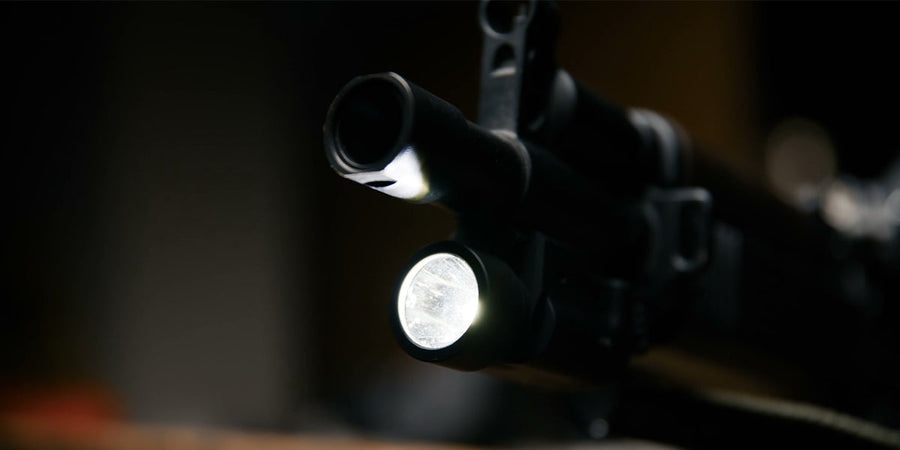 Close-up of a rifle barrel with a mounted flashlight in a dark scene