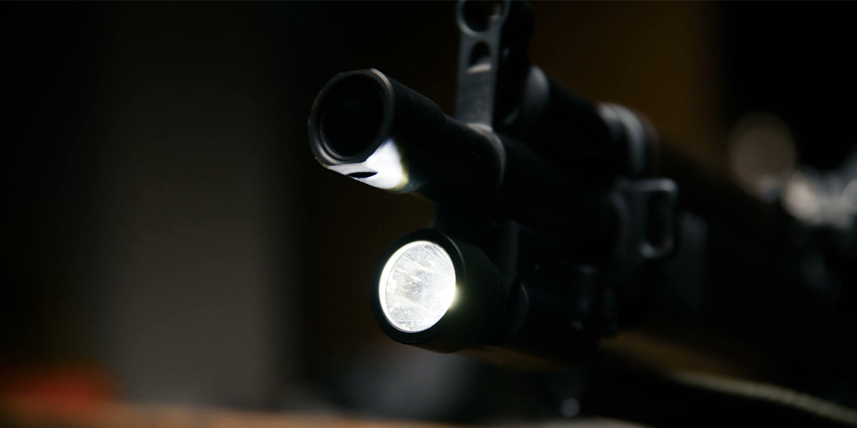 Close-up of a rifle barrel with a mounted flashlight in a dark scene