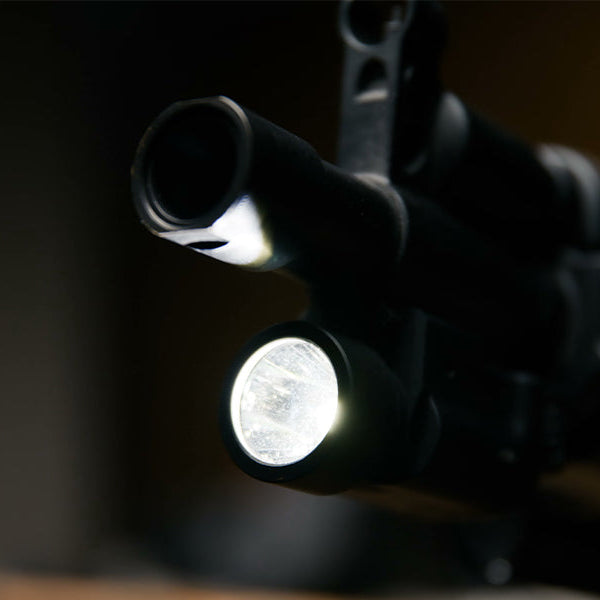 Close-up of a rifle barrel with a mounted flashlight in a dark scene