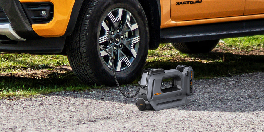 Portable tire inflator beside an orange pickup truck, connected to the front tire on a gravel road