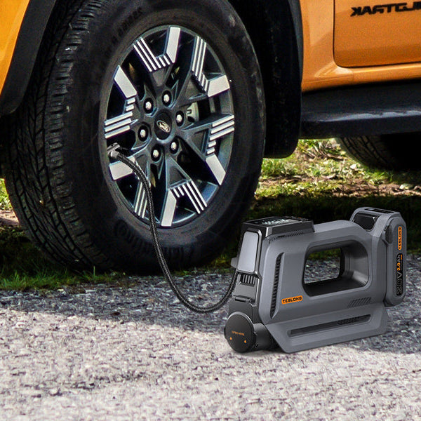 Portable tire inflator beside an orange pickup truck, connected to the front tire on a gravel road