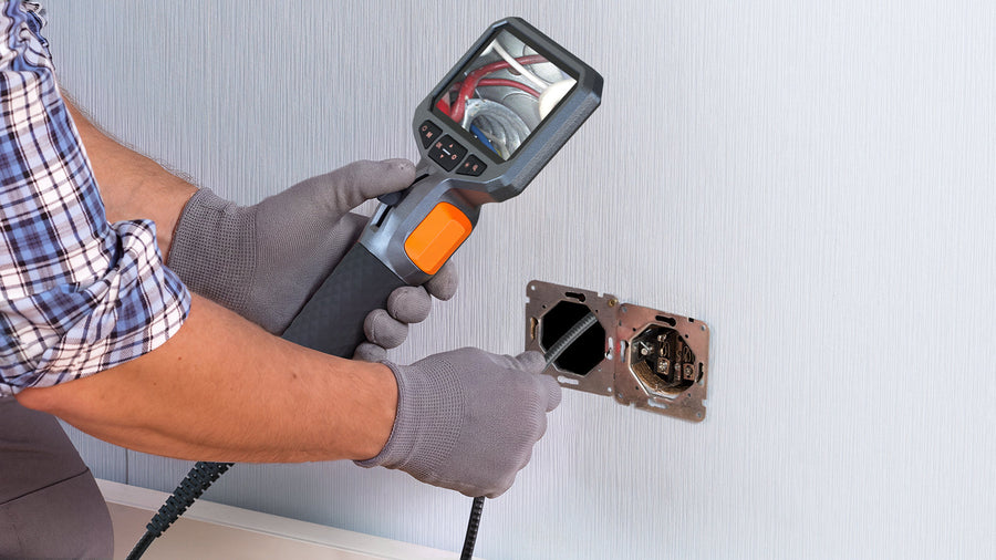 Worker using a borescope to inspect wiring inside a wall outlet.