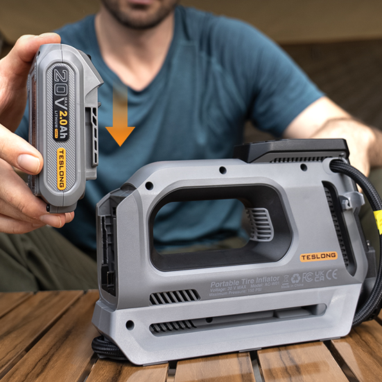 Man inserting a 20V lithium battery into a portable tire inflator at a campsite